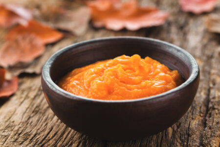 Fresh homemade pumpkin puree in bowl, colorful autumn leaves in the back (Selective Focus, Focus…